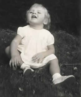 Louise sitting independently on the lawn in Kenya smiling as always
